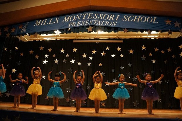 Children performing on stage beneath a Mills Montessori School banner